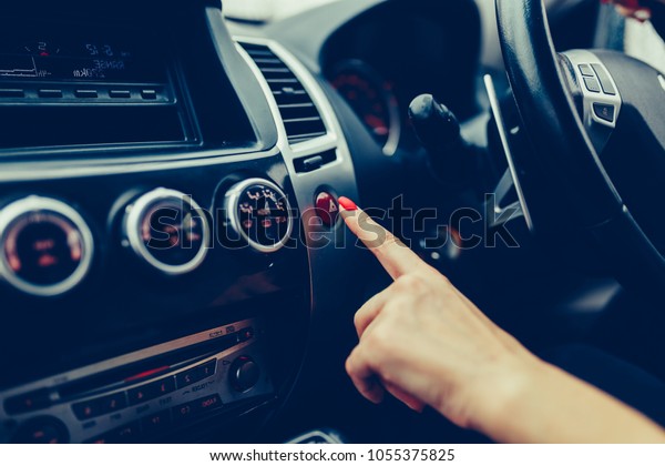 The female hand presses the button to turn the\
alarm into the car. Button emergency car lighting shot of a finger.\
Woman finger pressing emergency button on car dashboard. Stylish\
toned photo