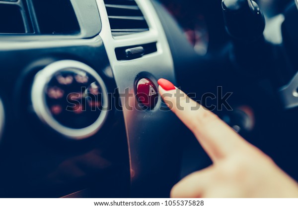 The female hand presses the button to turn the\
alarm into the car. Button emergency car lighting shot of a finger.\
Woman finger pressing emergency button on car dashboard. Stylish\
toned photo