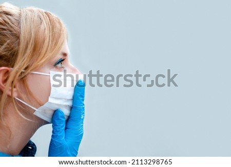 Female with hand in protective blue glove on mouth with surgical face mask. Responsible during Coronavirus pandemic or air Pollution. Close up profile portrait isolated on grey background. Copy space 
