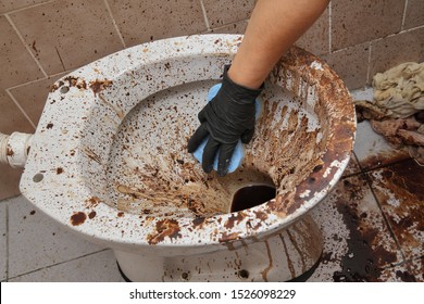Female hand in protective glove cleaning dirty toilet using sponge, messy toilet in a dirty bathroom, very bad condition