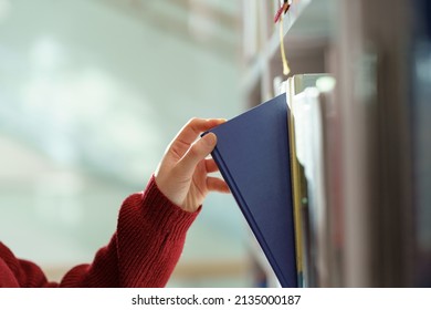 Female Hand Pulling Book From Bookshelf In Public Library In University, College Or High School. Woman Student Take Novel From Bookcase In Bookshop Store, Soft Focus. Education And Literature Concept