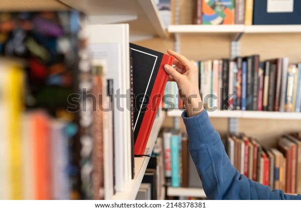 Female hand pulling book from bookshelf in public\
library in university, college or high school. Woman student take\
novel from bookcase in bookshop store, soft focus. Education and\
literature concept