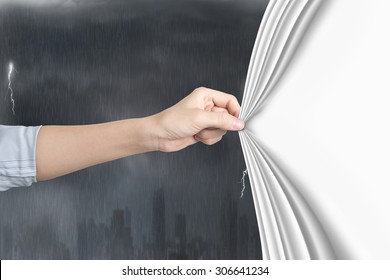 Female hand pulling open blank white curtain covering stormy city.