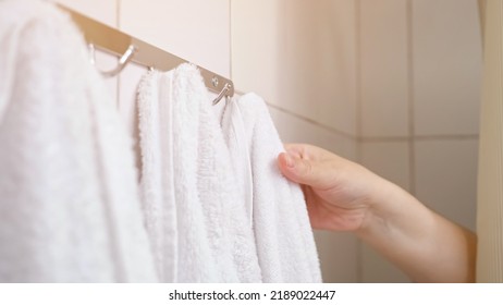 Female hand pulls back bath curtain and removes towel from hook. Woman takes terry towel after taking shower during morning routine, sunlight - Shutterstock ID 2189022447