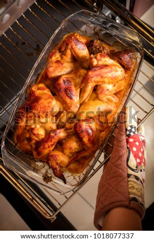 The female hand pulls out the chicken wings from the oven. Light from the oven lamp 