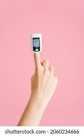 Female Hand With Pulse Oximeter On Index Finger On Pink Background. Vertical Foto