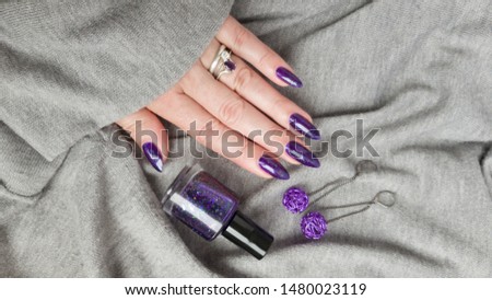 Female hand with purple long nails and nail polish bottle