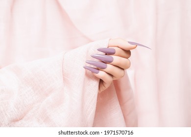 Female Hand With Purple Stiletto Nail Design. Long Nail Polish Manicure. Woman Hand On Glitter Pink Fabric Background.