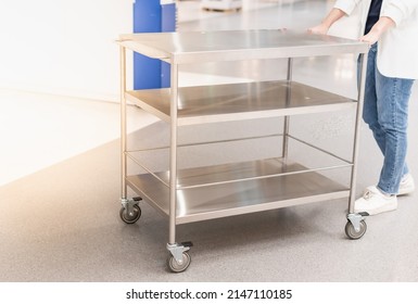 Female Hand Pushing The Stainless Steel Food Trolley Cart To Move A Lot Of Parcels. 