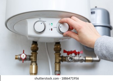 Female hand puts thermostat of electric water heater (boiler) in low low power consumption mode . Household enegry saving equipment