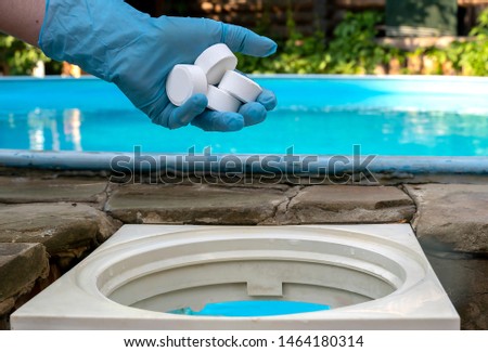 Female hand puts white tablets into pool skimmer. Cleaning, disinfection of water in the swimming pool.