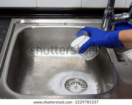 Female hand putting baking soda on drain in kitchen sink from glass jar. Close up. Eco friendly house cleaning concept.