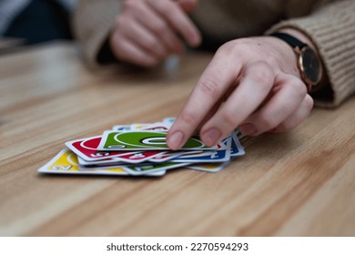 A female hand putting a card into a pile of colorful cards on a table - playing a card game. An indoor fun activity for long winter evenings, couple date idea, entertainment for friends concept
