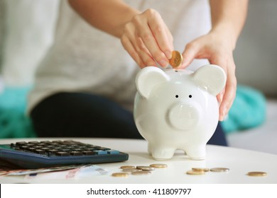 Female hand putting coin into piggy bank closeup