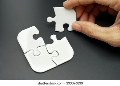 Female Hand Putting A Missing Piece And Solving White Jigsaw Puzzle Placed On Top Of Colour Background - Complete. Business, Challenge, Solution, Smart And Strategy Concept