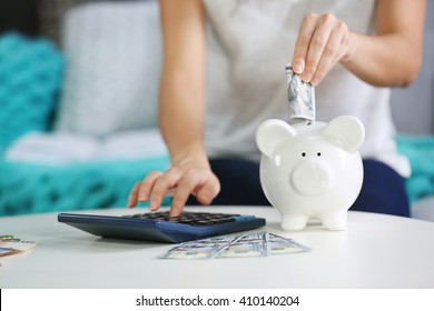 Female hand putting money into piggy bank and counting on calculator closeup