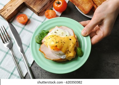 Female Hand Putting Plate With Tasty Egg Benedict On Table