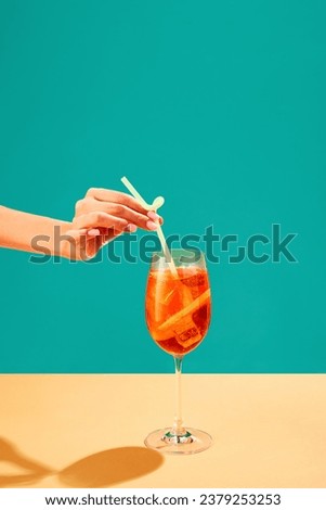 Female hand putting straw into Aperol spritz cocktail isolated over green background. Refreshment, aperitif. Concept of alcohol drinks, party, holidays, bar, mix. Poster. Copy space for ad
