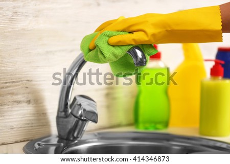 Female hand with rag cleaning a tap in the kitchen