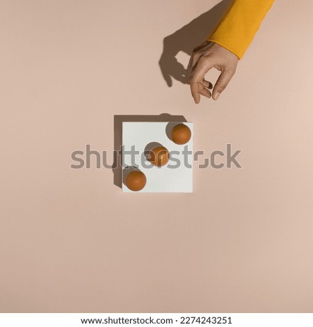 Female hand reaching for three fresh brown chicken eggs on white rectangle stand. Minimal food concept. Flat lay.