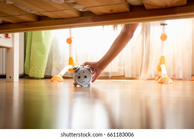 Female Hand Reaching Under The Bed For Alarm Clock