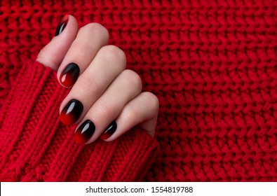 Female hand and red black ombre gradient nails in sweater  Trendy winter manicure concept 