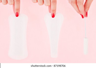 Female Hand With Red Fingernails Holding A Clean Pantyliner, G - String Pantyliner And A Tampon Isolated Over Pink Background. Feminine Hygiene Concept.