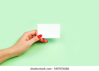 Female Hand With Red Manicure Holding Blank White Business Card, Close-up, Isolated On Green Background