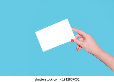 A female hand with a red manicure holds a blank white mockup for a flyer or postcard on a blue background. Female hands hold a blank sheet of paper on a yellow background. Advertising space - Shutterstock ID 1912837051
