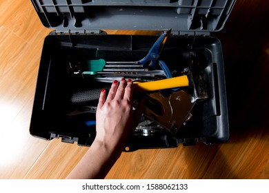 Female Hand With Red Manicure Reaches For Tools In An Open Tool Box, View From The Top