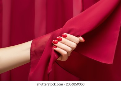 Female hand with red nail design. Glitter red nail polish manicure. Woman hand hold red fabric on red fabric background.