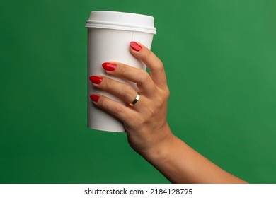 Female hand with red nail polish holding paper cup on a green background.
