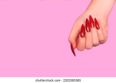 Female hand with red stiletto nail design. Glitter red nail polish manicure. Female hand with stiletto nails on pink background. Copy space. Plce for text.