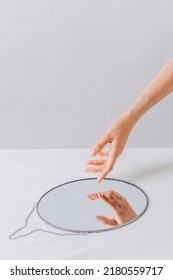 Female Hand And Its Reflection In Mirror. Mirror Resting On Surface On White Background.