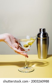 Female hand with rings holds glass of martini cocktail with olives. Focus on shadows