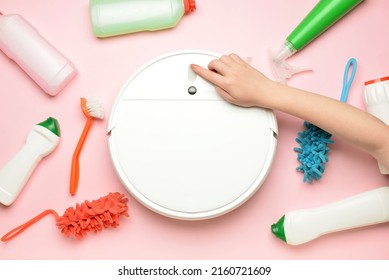 Female Hand, Robot Vacuum Cleaner And Cleaning Supplies On Pink Background