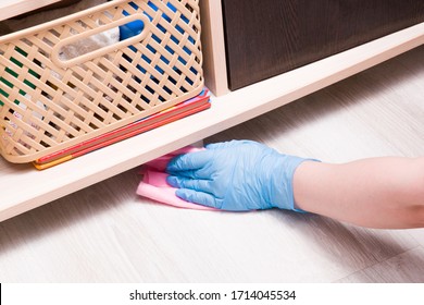 A Female Hand In A Rubber Disposable Glove With A Pink Rag Wipes Dust Under The Closet, On The Shelf Is A Basket Of Cigars And A Children's Book, Cleaning The Children's Room