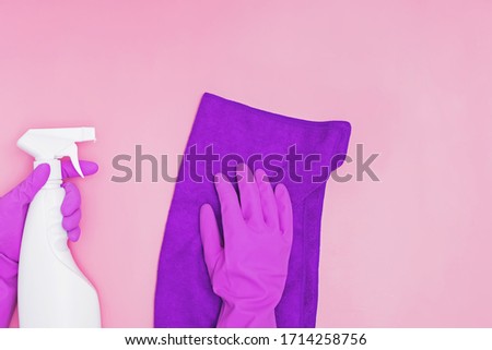 Female hand in rubber glove holding cleaning spray and rag on pink background. Cleaning, desinfection concept.