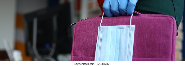 Female Hand With Safety Gloves Hold Mask And Laptop Bag Against Office Closeup Background