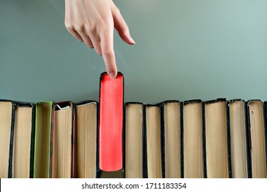 A Female Hand Selects A Brightly Red Book To Read From A Series Of Books. Top View, Close Up