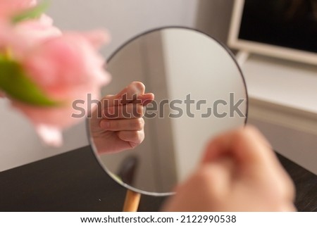 Female hand is showing a Fig gesture. Reflection in the mirror. Close-up