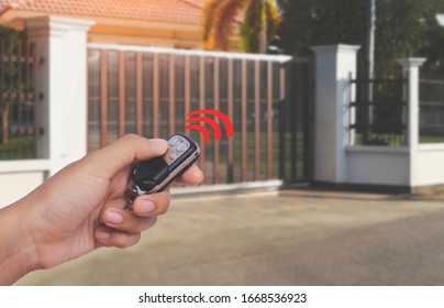 Female hand showing and using remote control to open or close the automatic wooden gate with home blurred background. Security and save time concept.