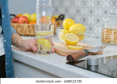 Female Hand With Slice Of Lemon In Kitchen, With Freshly Made Drink Sparkling Water With Lemon