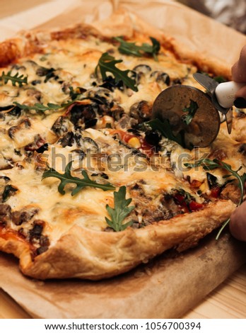 Female hand slicing delicious pizza with cheese, ruccola and olives
