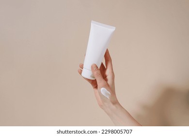Female hand with smear holding blank mockup tube of cream on beige isolated background. Daily skincare and body care routine. Image for your design - Shutterstock ID 2298005707