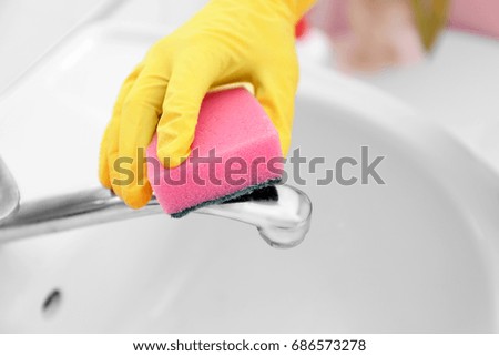 Female hand with sponge cleaning a tap in the bathroom