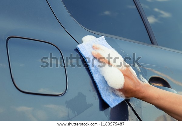 A female hand with a sponge in a soapy foam washes\
the car