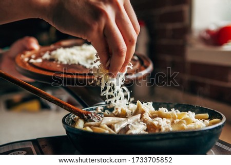 Female hand sprinkles grated cheese on a pan with pasta