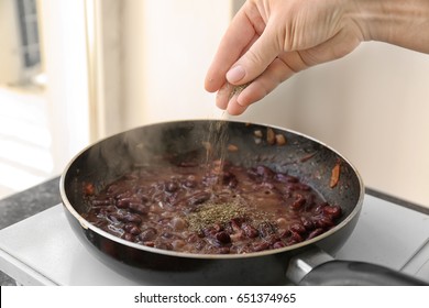 Female Hand Sprinkling Herbs On Beans In Frying Pan