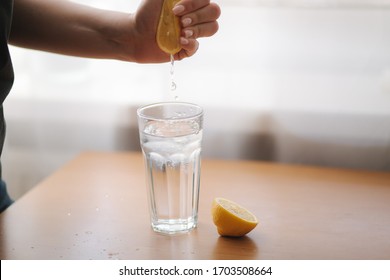 Female Hand Squeeze Lemon Juice In Glass With Water. Water With Lemon. Fresh Drink On Quarantine